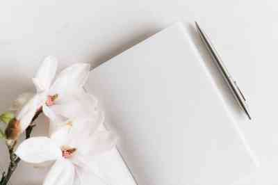 Cuaderno en blanco con flores blancas encima y bolígrafo plateado a un lado